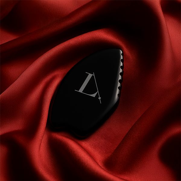 Gua sha en obsidienne noire de la marque LimeLife by Alcone. Photo produit sur fond de satin rouge