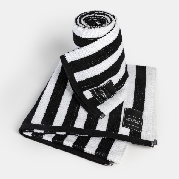 Ensemble de serviettes éponges à rayures noires et blanches, avec une serviette roulée posée sur une autre pliée, sur fond blanc.