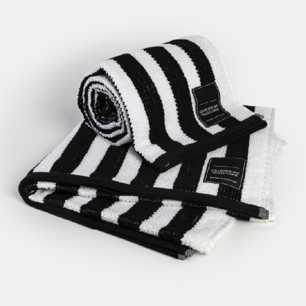Vue d'angle d'une serviette de bain à rayures noires et blanches roulée sur une serviette pliée, mettant en avant le motif et la texture.