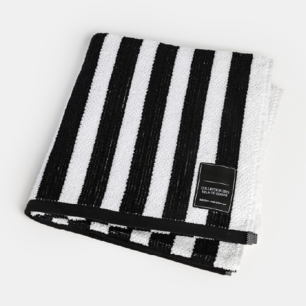 Serviette éponge premium pliée en carré, montrant les rayures verticales noires et blanches, la bordure et l'étiquette noire.