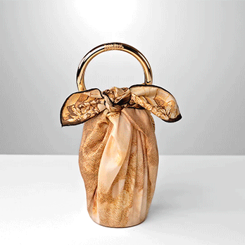 Packaging cadeau haut de gamme, bouteille élégamment enveloppée dans un tissu imprimé doré façon furoshiki, avec anse circulaire en métal doré.