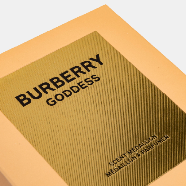 Gros plan sur le couvercle du boîtier Burberry Goddess, montrant le logo en noir sur une étiquette dorée texturée rappelant le grain du trench iconique.