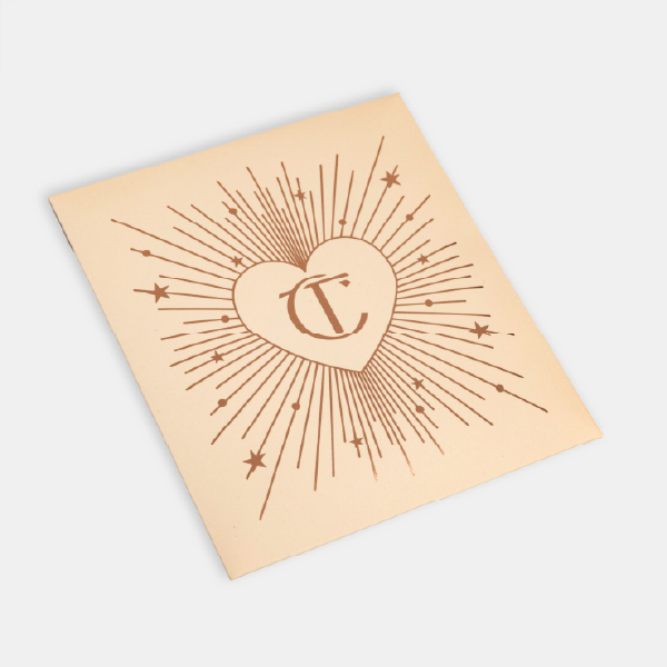 La carte de présentation de la houppette, montrant le design d'un cœur avec le monogramme CT entouré d'étoiles et de rayons.