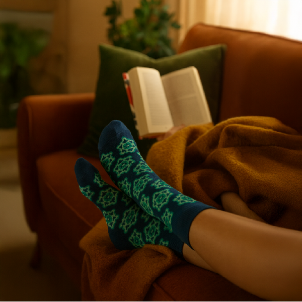 Personne portant les chaussettes bleues à motifs ski rétro Glowria, relaxant sur un canapé avec un plaid et un livre, illustrant leur confort.