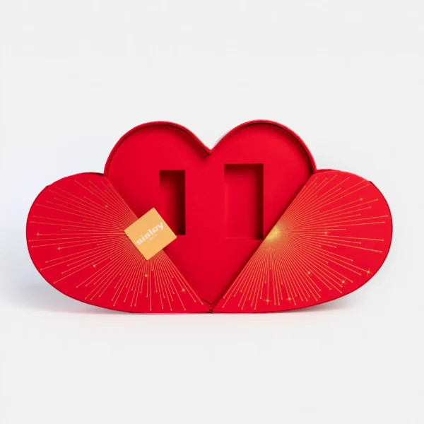 Coffret cadeau Sisley en forme de cœur rouge avec ouverture à volets, décoré de motifs dorés rayonnants, présenté ouvert avec emplacements intérieurs pour produits beauté.