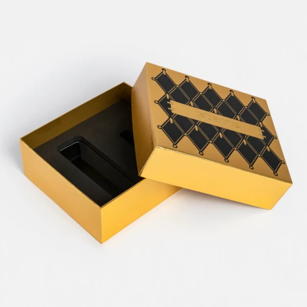 Coffret doré Rabanne au design géométrique noir et or, avec intérieur en mousse de protection, présenté ouvert sur fond blanc.