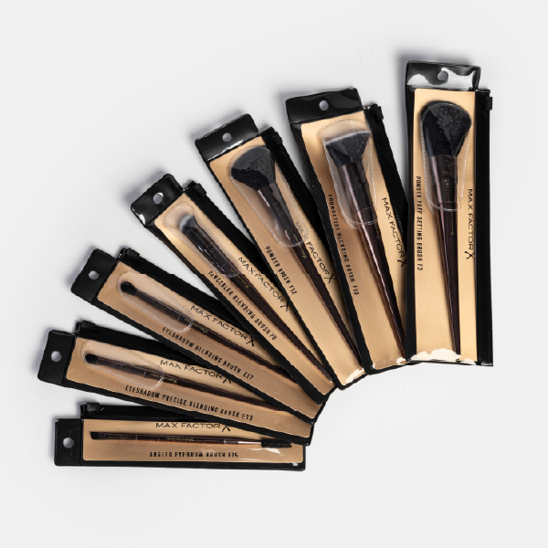 La collection complète des pinceaux Max Factor X, chacun dans sa pochette de vente individuelle, disposée en éventail.