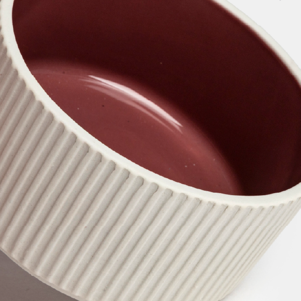 Gros plan sur une coupelle en porcelaine, mettant en évidence le contraste entre l'intérieur laqué brillant de couleur bordeaux et l'extérieur mat et strié.