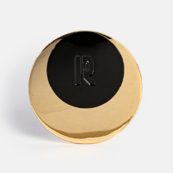 Gros plan sur le dos du miroir Rabanne montrant le design en métal doré poli, le médaillon central en laque noire et le monogramme "R" en relief.