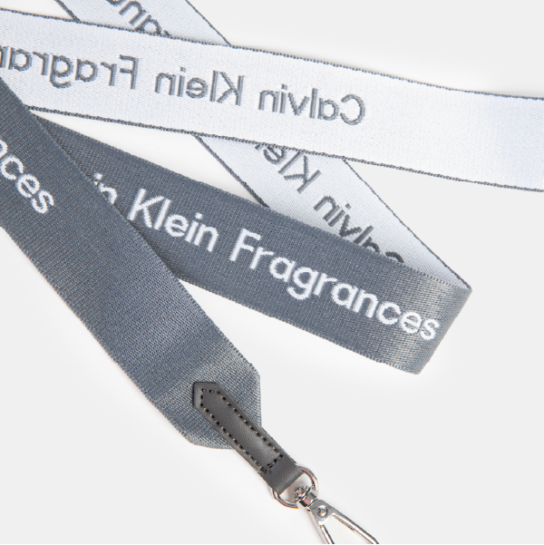 Gros plan sur la sangle tissée bicolore de la gourde, montrant le logo "Calvin Klein Fragrances" et le détail du mousqueton en métal.