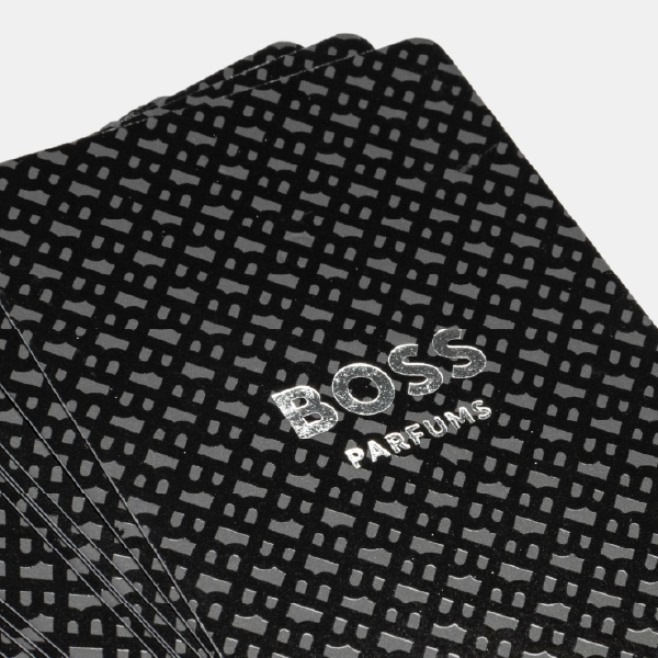 Gros plan sur le dos des cartes à jouer BOSS, montrant le motif monogramme ton sur ton et le logo "BOSS PARFUMS" en argenté.