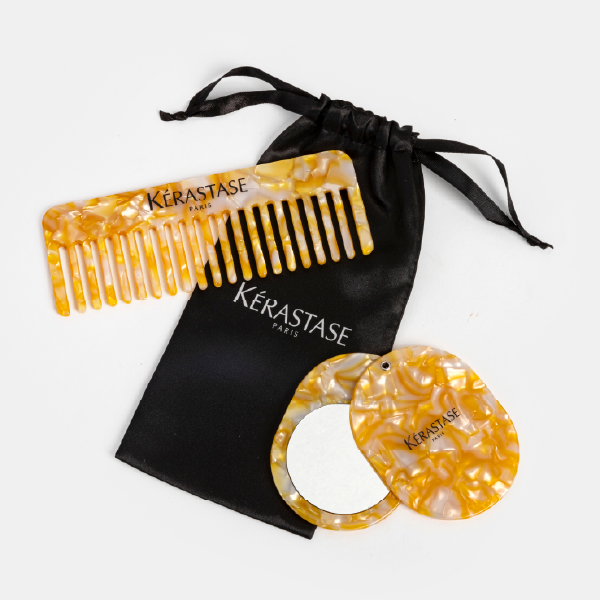 Le set beauté Kérastase Elixir Ultime, comprenant un peigne et un miroir de poche en acétate à effet marbré doré, présentés avec leur pochette en satin noir.