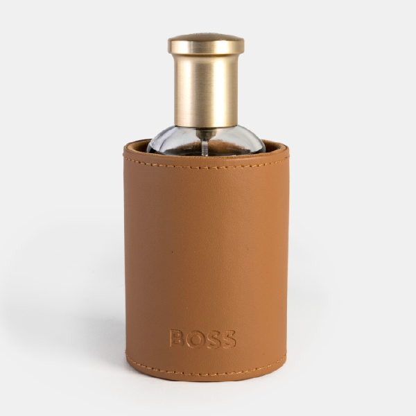 Le flacon de parfum BOSS Bottled inséré dans son fourreau rigide effet cuir de couleur camel, avec le bouchon doré qui dépasse élégamment.