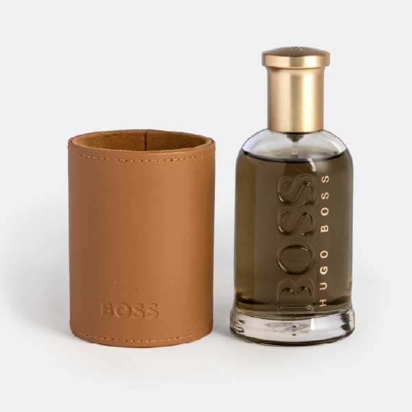 Le fourreau rigide en effet cuir camel posé à côté du flacon de parfum BOSS Bottled, montrant les deux éléments séparément.
