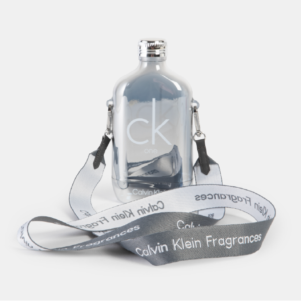 Gourde réutilisable Calvin Klein au fini chromé argenté, design inspiré du flacon CK ONE, présentée avec sa sangle de transport grise et blanche.