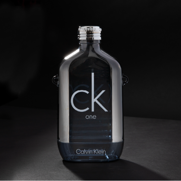 La gourde Calvin Klein sans sa sangle, sur fond noir pour mettre en valeur sa finition chromée argentée et sa forme iconique de flacon de parfum.