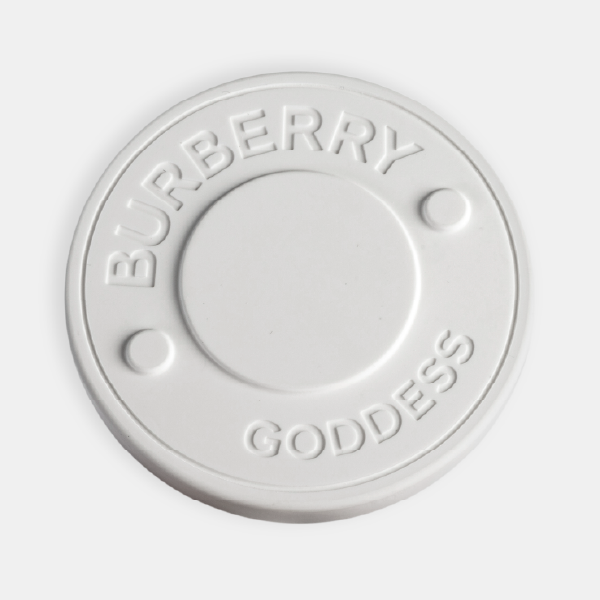 Gros plan sur le médaillon en céramique blanc mat, montrant le logo et le nom "Burberry Goddess" en relief avec une grande précision.