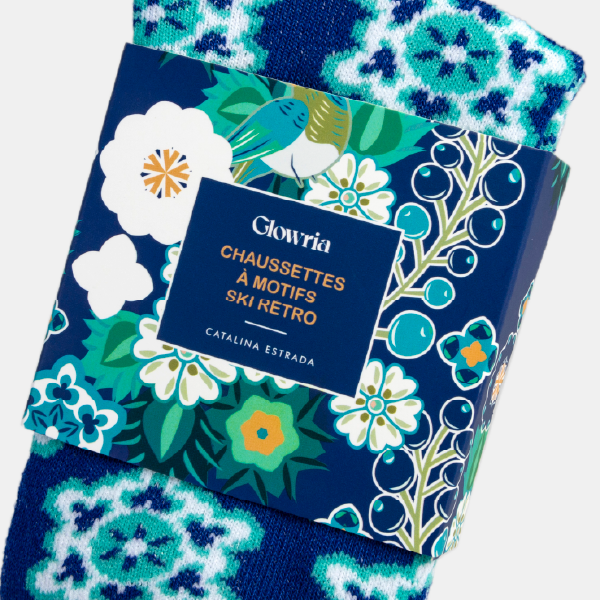 Gros plan sur l'étui illustré des chaussettes Glowria, montrant le design floral, l'oiseau de Catalina Estrada et l'inscription "Chaussettes à motifs ski rétro".