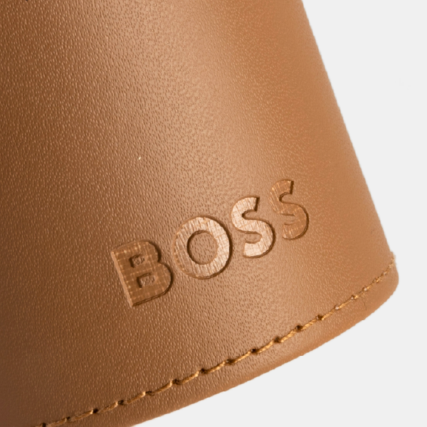 Gros plan sur le logo "BOSS" embossé sur le fourreau effet cuir de couleur camel, montrant la texture grainée et la couture ton sur ton.