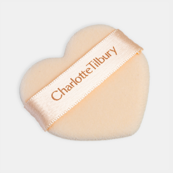 La houppette de maquillage en forme de cœur Charlotte Tilbury, avec sa texture velours couleur pêche et son ruban en satin siglé.