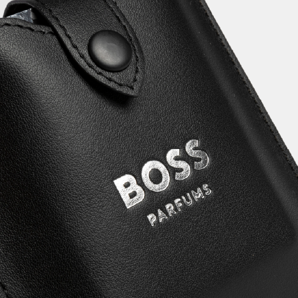 Gros plan sur le logo "BOSS PARFUMS" en marquage à chaud argenté sur la texture du porte-cartes noir.