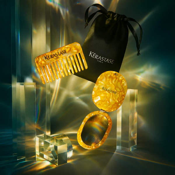 Mise en scène luxueuse du set Kérastase Elixir Ultime, avec le peigne, le miroir et la pochette flottant parmi des blocs de verre et des reflets dorés.