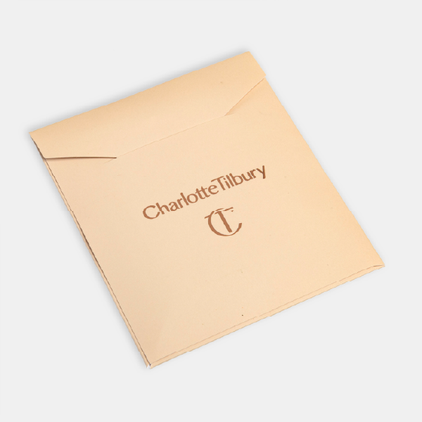 La pochette en papier de couleur pêche pour la houppette, avec le logo Charlotte Tilbury et le monogramme CT imprimés.