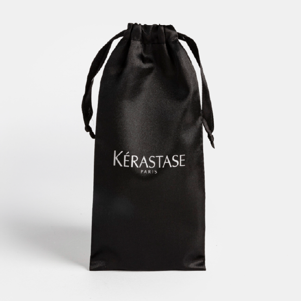 Vue de la pochette en satin noir Kérastase présentée debout, fermée, montrant son volume et son aspect soyeux.