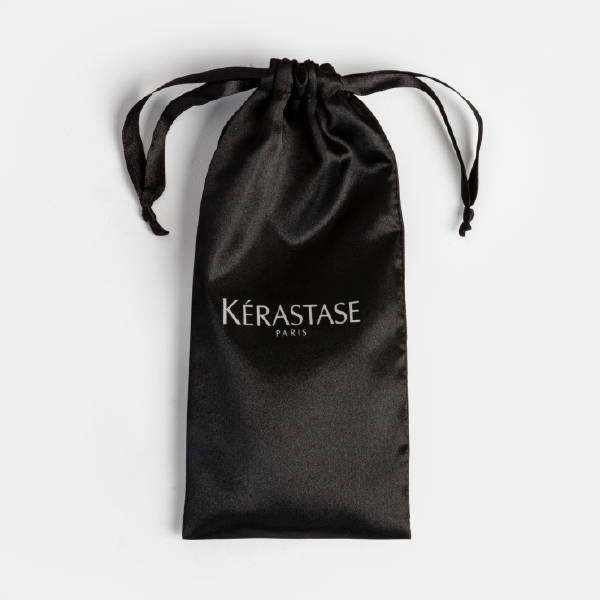 La pochette en satin noir de l'ensemble Kérastase Elixir Ultime, posée à plat avec son cordon de serrage et le logo blanc "Kérastase Paris".