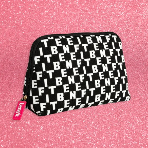 Trousse de maquillage Benefit en maille noire et blanche à motif logo répétitif, avec curseur rose vif, posée sur un fond scintillant rose.